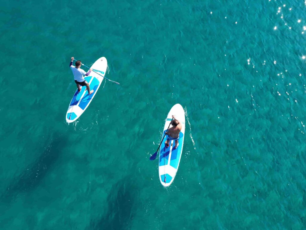 Two people paddleboarding on clear turquoise water in the Algarve, Portugal