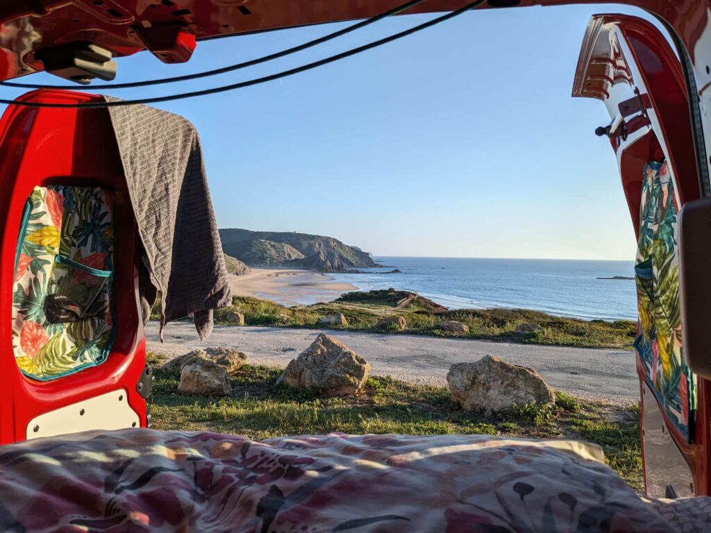 View of a beach and ocean from inside a campervan with open back doors