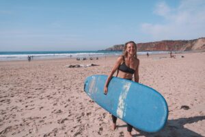 Surfer carrying a rented surfboard on an Algarve beach near Faro, with cliffs in the background