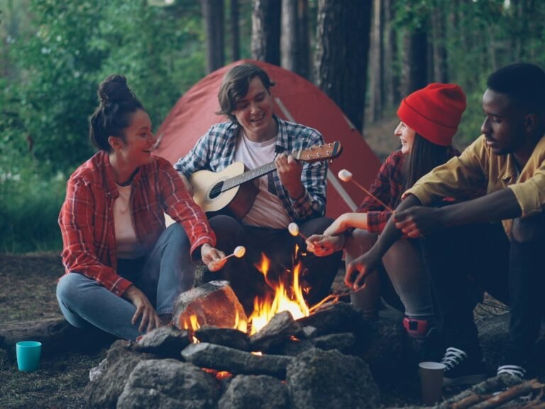 Friends playing guitar around a campfire next to a tent